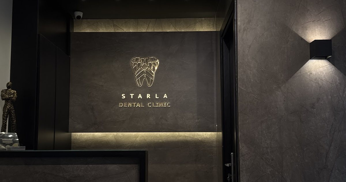 استقبال عيادة ستارلا: مكتب من الحجر الداكن، وشعار ستارلا الذهبي مضاء على الحائط ورا المكتب.